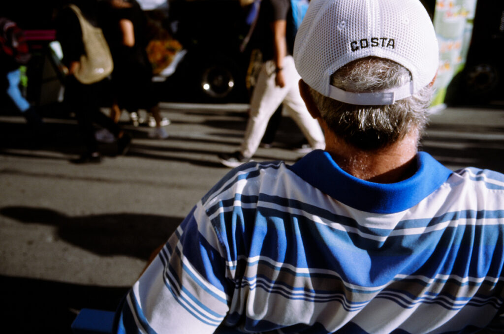 An older man leaning back on a rail watching people walking by at the CNE, the Ex, the Canadian National Exhibition.