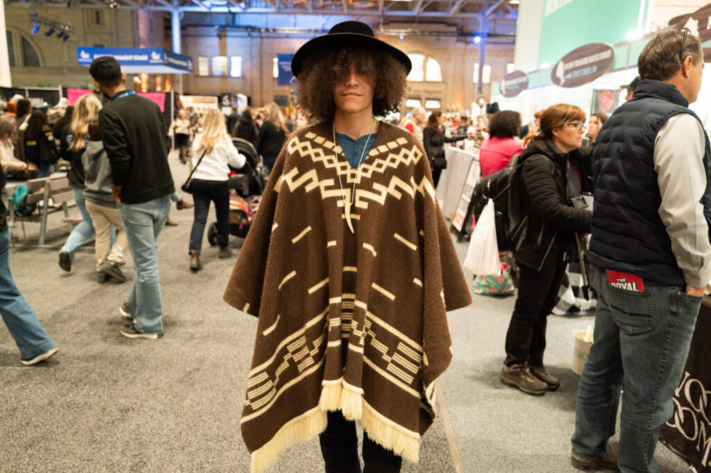 A fashionable young man in a wool poncho and a hat posing for a portrait at The Royal Agricultural Winter Fair in Toronto.