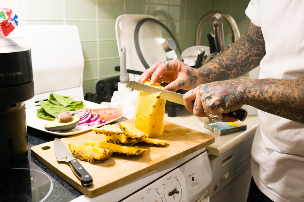 Chino is cutting a pineapple in the kitchen at Crows Nest Barbershop in Kensington Market in Toronto.